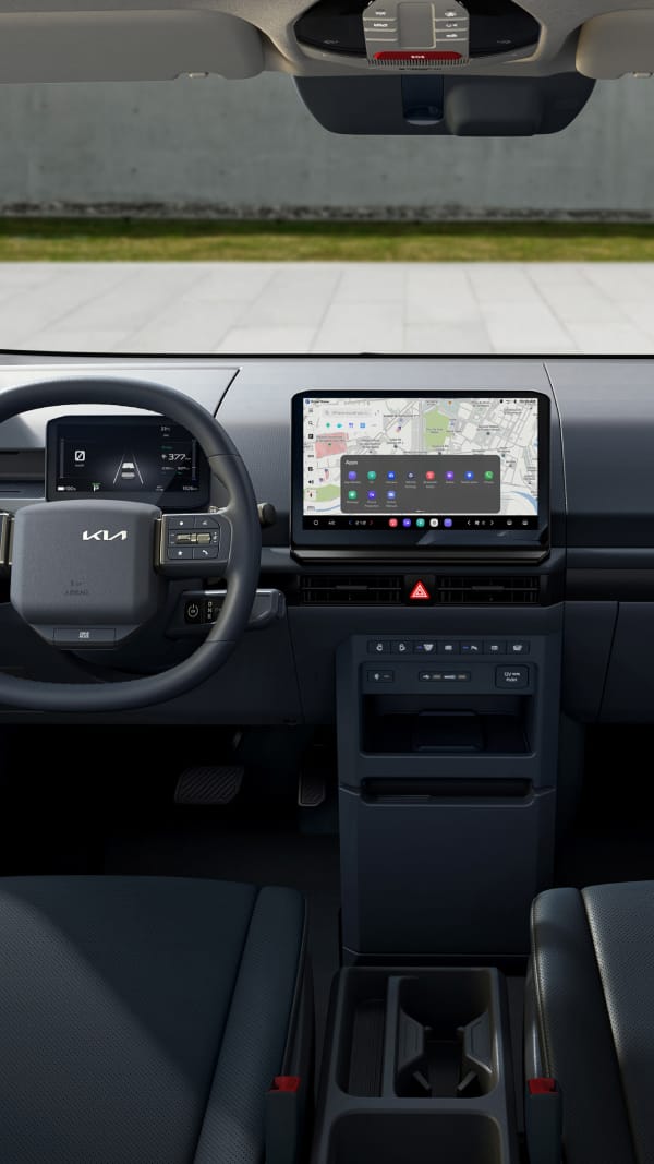 Fahrerbereich des Kia PV5 WAV mit Lenkrad, digitalem Kombiinstrument, zentralem Display und Cockpit-Layout